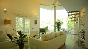 Una sala de estar moderna con una mesa de centro de vidrio, un sofá blanco, un televisor y una escalera que conduce a un nivel superior.