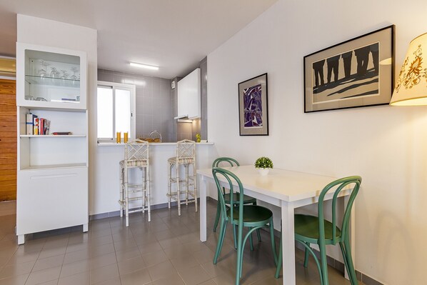 A modern kitchen with white cabinets, a dining area with a white table and green chairs, and a framed artwork on the wall. - Beachfront apartment in Puerto de Pollensa (Port de Pollença)