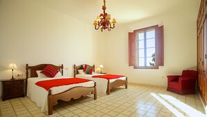 A hotel room with two wooden beds, a red chair, a chandelier, and a window with curtains. - Holiday home 10 minutes from Palma, ideal for large groups (Llucmajor)