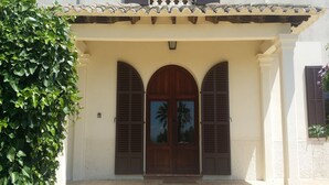 A building with a traditional architectural style, featuring a tiled roof, a wooden door with two arched windows, and a white wall. - Holiday home 10 minutes from Palma, ideal for large groups (Llucmajor)