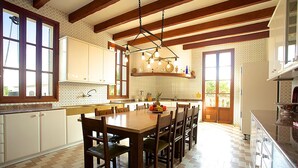 A spacious kitchen with wooden beams, a large dining table, and a fruit bowl on the table. - Holiday home 10 minutes from Palma, ideal for large groups (Llucmajor)