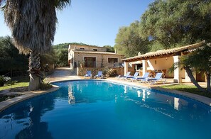 Une piscine avec des chaises longues et un bâtiment doté d’un toit en tuiles.