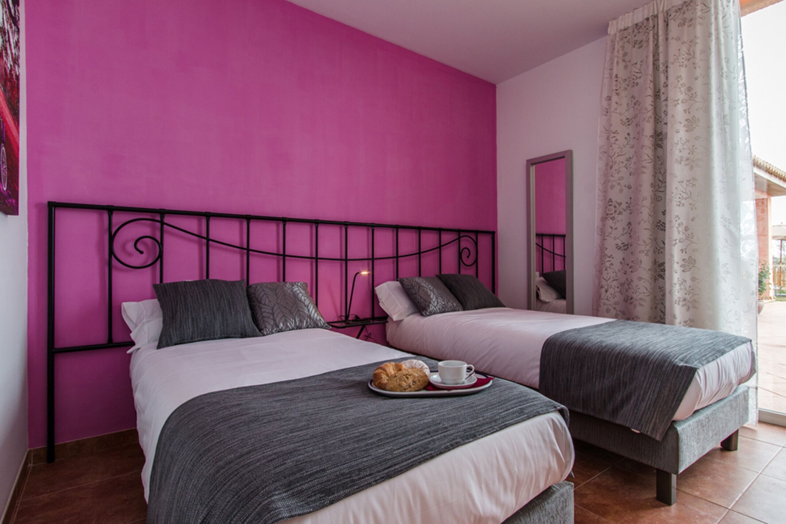 Habitación con dos camas, una pared rosa y una ventana con cortinas.