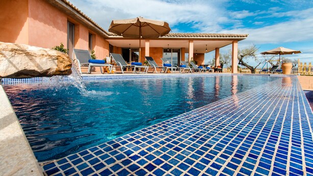 A swimming pool with blue mosaic tiles, lounge chairs, and umbrellas.