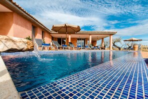 Una piscina con piastrelle blu a mosaico, lettini e ombrelloni.