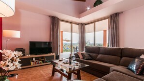 A modern living room with a flat-screen TV, a sofa, a coffee table, and a bookshelf.