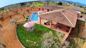 A villa with a swimming pool, outdoor seating, and a view of the surrounding countryside.