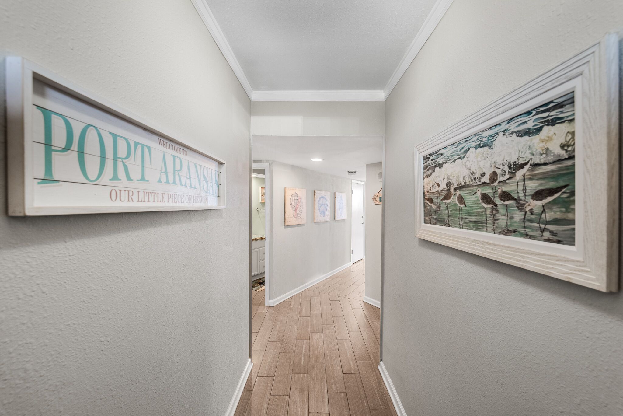 A hallway with a sign reading "PORT ARANS OUR LITTLE PIECE OF FISHING," framed artwork, and a wooden floor.