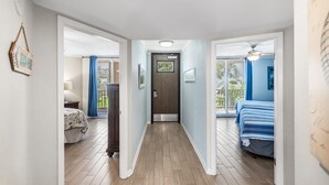A hallway with a wooden floor, a door at the end, and two bedrooms with beds and curtains. - Sea Gull #103: Beachfront 2 Bedroom 2 Bathroom With Spectacular Views and 24 Hour Management (Port Aransas)