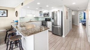 A modern kitchen with white cabinets, stainless steel appliances, and a granite island with bar stools. - Sea Gull #103: Beachfront 2 Bedroom 2 Bathroom With Spectacular Views and 24 Hour Management (Port Aransas)