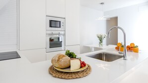 A modern kitchen with white cabinetry, a stainless steel sink, and a woven placemat with bread, cheese, and tomatoes. - Urban style vacation home in S'Illot 5 minutes from Sa Coma and Cala Morlanda (S´illot-Cala morlanda)