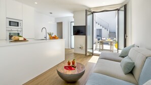 A modern kitchen with a built-in microwave and oven, a dining area with a round wooden table, and a living room with a sofa and a large window. - Urban style vacation home in S'Illot 5 minutes from Sa Coma and Cala Morlanda (S´illot-Cala morlanda)