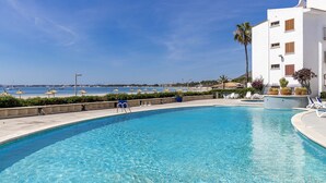 A clear blue pool with lounge chairs and umbrellas, a white building, and a view of the sea. - 1st line apartment Alcudia beach CAB (Puerto de Alcudia)