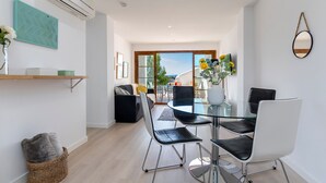 A modern dining area with a glass table and chairs, a wicker basket, and a wall-mounted air conditioner. - 1st line apartment Alcudia beach CAB (Puerto de Alcudia)