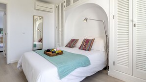 A bedroom with a bed, a bedside lamp, a mirror, and a window with shutters. - 1st line apartment Alcudia beach CAB (Puerto de Alcudia)