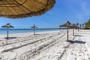 A beach with thatched umbrellas and a clear blue sky.