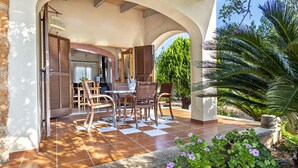 An outdoor patio with a checkered floor, wooden furniture, and a stone planter with flowers. - Country house with amazing swimming pool and garden in a beautiful rural setting (Campanet)