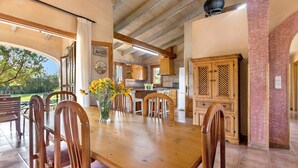 A dining area with a wooden table and chairs, a vase with flowers, and a view of the outdoors. - Country house with amazing swimming pool and garden in a beautiful rural setting (Campanet)