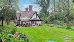 Une maison de style Tudor dotée d’un jardin bien entretenu, d’une terrasse avec des meubles d’extérieur et d’une cheminée bien visible.