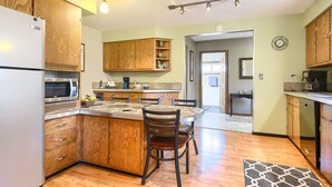 Una cocina con armarios de madera, un refrigerador, un microondas y una zona de comedor con sillas y una mesa.