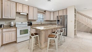 A modern kitchen with light wood cabinets, a central island with bar stools, stainless steel appliances, and a staircase leading to another level. - 2-min Walk to Beach, Private House with Heated Pool (South Padre Island)