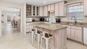 A modern kitchen with a central island, bar stools, a built-in oven, and a window with blinds. - 2-min Walk to Beach, Private House with Heated Pool (South Padre Island)