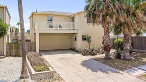 A two-story house with a garage, a balcony, and a well-maintained garden with palm trees and shrubs. - 2-min Walk to Beach, Private House with Heated Pool (South Padre Island)