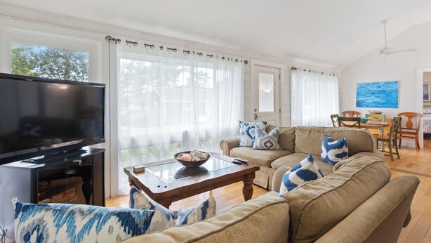 A living room with a sofa, a coffee table, a TV, and a dining area with chairs and a table. - Rex- East Hampton Cottage- 5 stars (East Hampton)