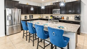 A modern kitchen with dark cabinets, stainless steel appliances, a granite countertop, and blue bar stools.