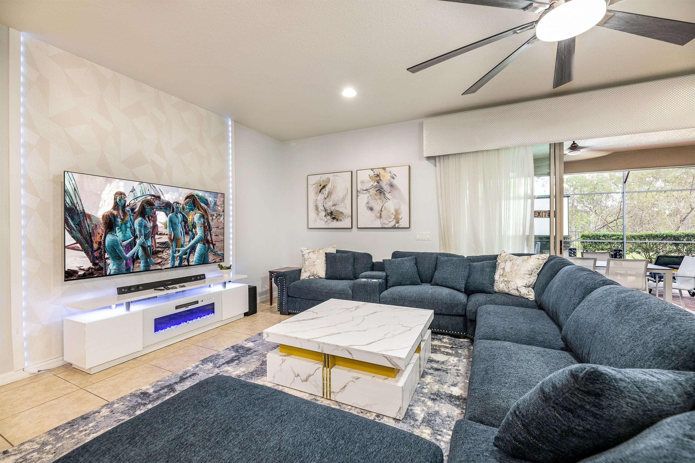 A modern living room with a sectional sofa, a flat-screen TV, a ceiling fan, and artwork on the walls.