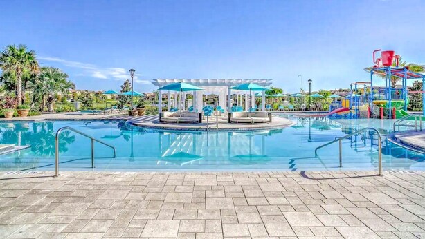 A swimming pool with a sunken seating area, surrounded by palm trees and a water slide.