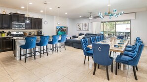 A modern kitchen with dark cabinets, a central island with bar stools, and a dining area with blue upholstered chairs and a wooden table.