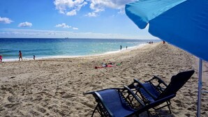 Une plage avec un parasol bleu, une chaise et un rivage sablonneux.