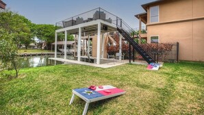 Una terraza moderna al aire libre con piscina, rodeada de césped y un pequeño estanque.