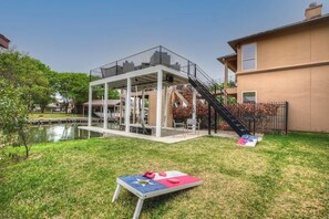 Une terrasse extérieure moderne avec une piscine, entourée d’une pelouse et d’un petit étang.