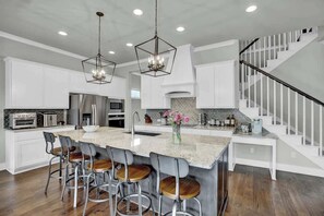 A spacious kitchen with a large island, bar stools, and pendant lighting.
