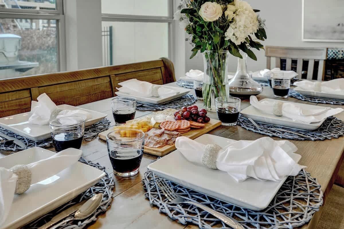Una mesa de comedor dispuesta con platos, vasos, cubiertos y un centro de mesa con flores blancas.