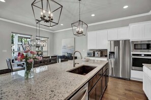 Une cuisine moderne dotée d’un grand îlot central, d’appareils électroménagers en acier inoxydable et de luminaires suspendus.