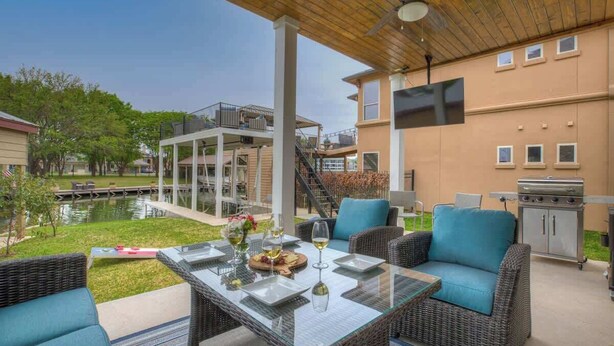 Un patio al aire libre con una mesa de vidrio, muebles de mimbre y una parrilla.