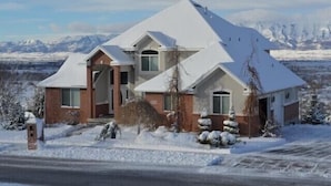Ein zweistöckiges Haus mit schneebedecktem Dach und einer Bergkulisse.