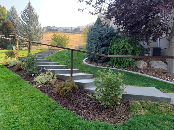 A residential property with a concrete staircase leading to a house, surrounded by well-maintained grass, shrubs, and trees. - Entire Basement, Private Entrance, Gorgeous Views (North Logan)