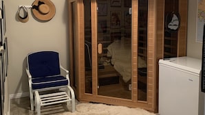Ein Zimmer mit blauem Sessel, Holzschrank und weißem Kühlschrank.