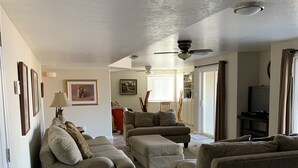 Ein Wohnzimmer mit beigen Sofas, einem Teppich und einem Deckenventilator.