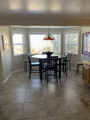 Enjoy meals in this dining area with a round table and six chairs, surrounded by a large window and a decorative light fixture.
