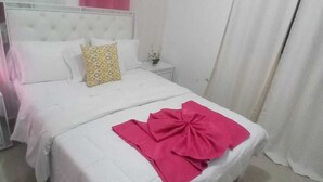 A hotel room with a large bed, white bedding, a nightstand with a lamp, and pink curtains. - LUXURY APARTMENT WITH JACUZZI, 5MINUTES FROM THE BEACH (Residencial Romana)