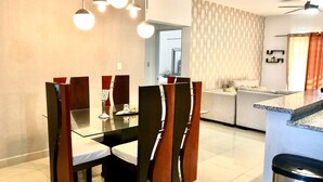 A modern dining area with a glass table and wooden chairs, a kitchen with a granite countertop, and a patterned wall in the background. - LUXURY APARTMENT WITH JACUZZI, 5MINUTES FROM THE BEACH (Residencial Romana)