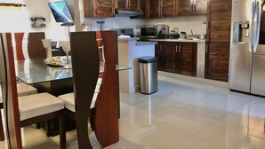A modern kitchen with wooden cabinets, stainless steel appliances, a glass dining table, and a TV. - LUXURY APARTMENT WITH JACUZZI, 5MINUTES FROM THE BEACH (Residencial Romana)