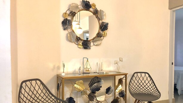 A room with a round mirror, two chairs, a console table, and decorative foliage. - LUXURY APARTMENT WITH JACUZZI, 5MINUTES FROM THE BEACH (Residencial Romana)