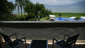 Un balcón con dos sillas y una mesa, con vista a una piscina y al mar y las montañas.