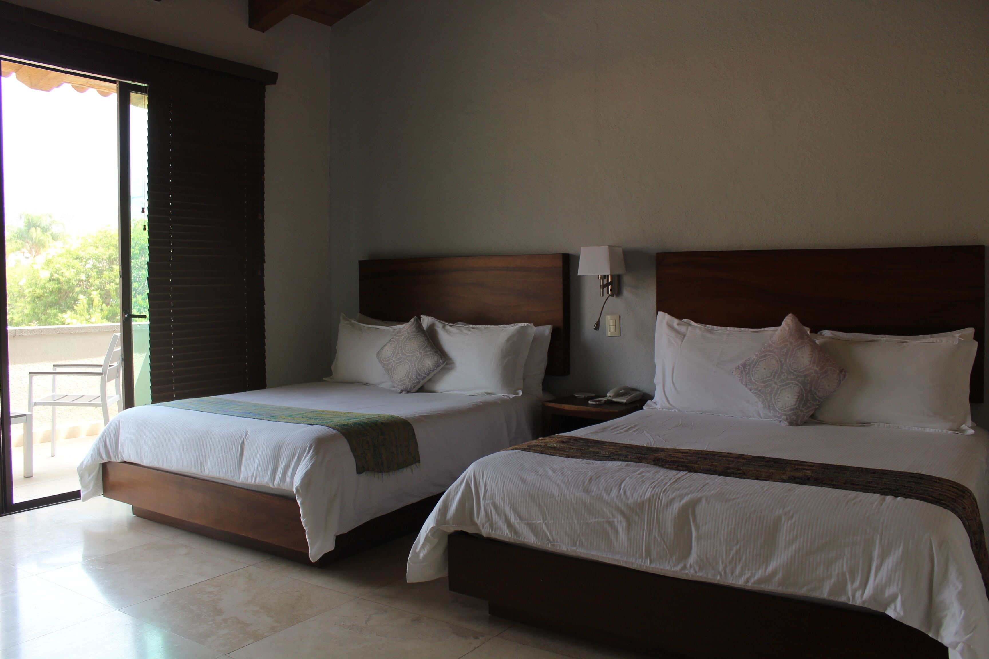 Dos camas con cabeceras de madera, ropa de cama blanca y una mesita de noche con una lámpara.